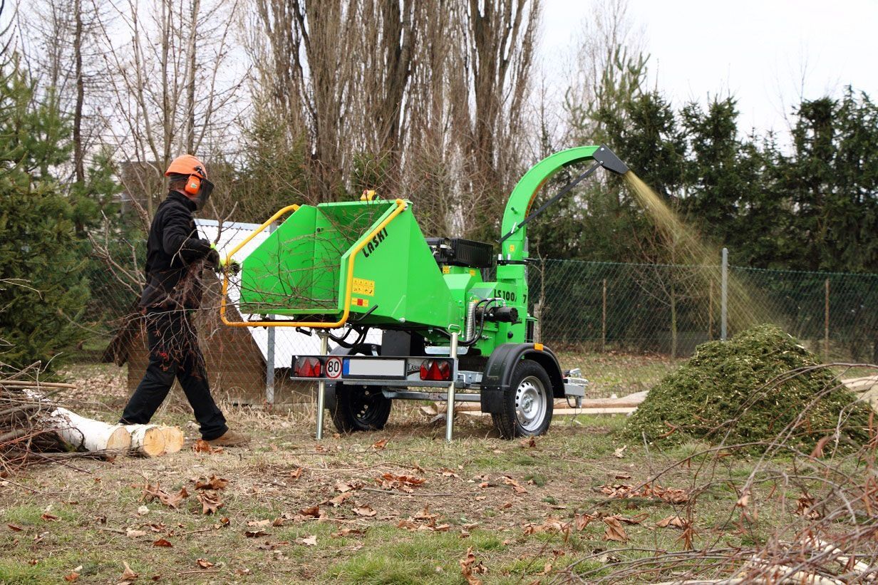 Ein Mann steht neben einer grünen Maschine, die Holz zerkleinert.
