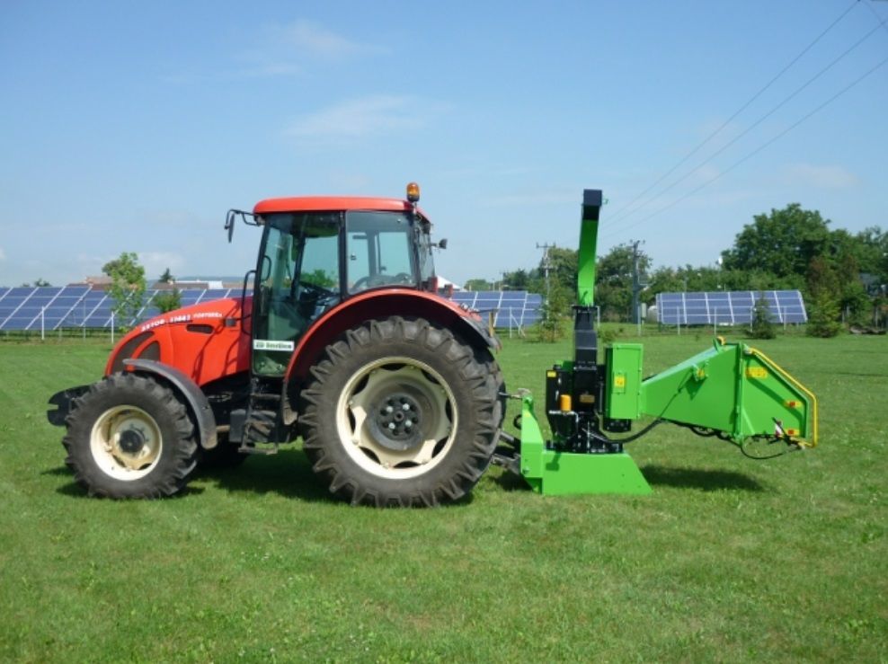 Ein roter Traktor mit einem daran befestigten grünen Häcksler steht auf einer Wiese.