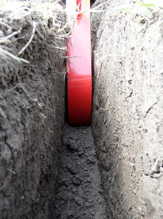 In einem Graben liegt ein rotes Rohr im Dreck.