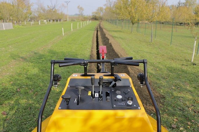 Ein gelber Traktor fährt auf einem Feld einen Feldweg entlang.