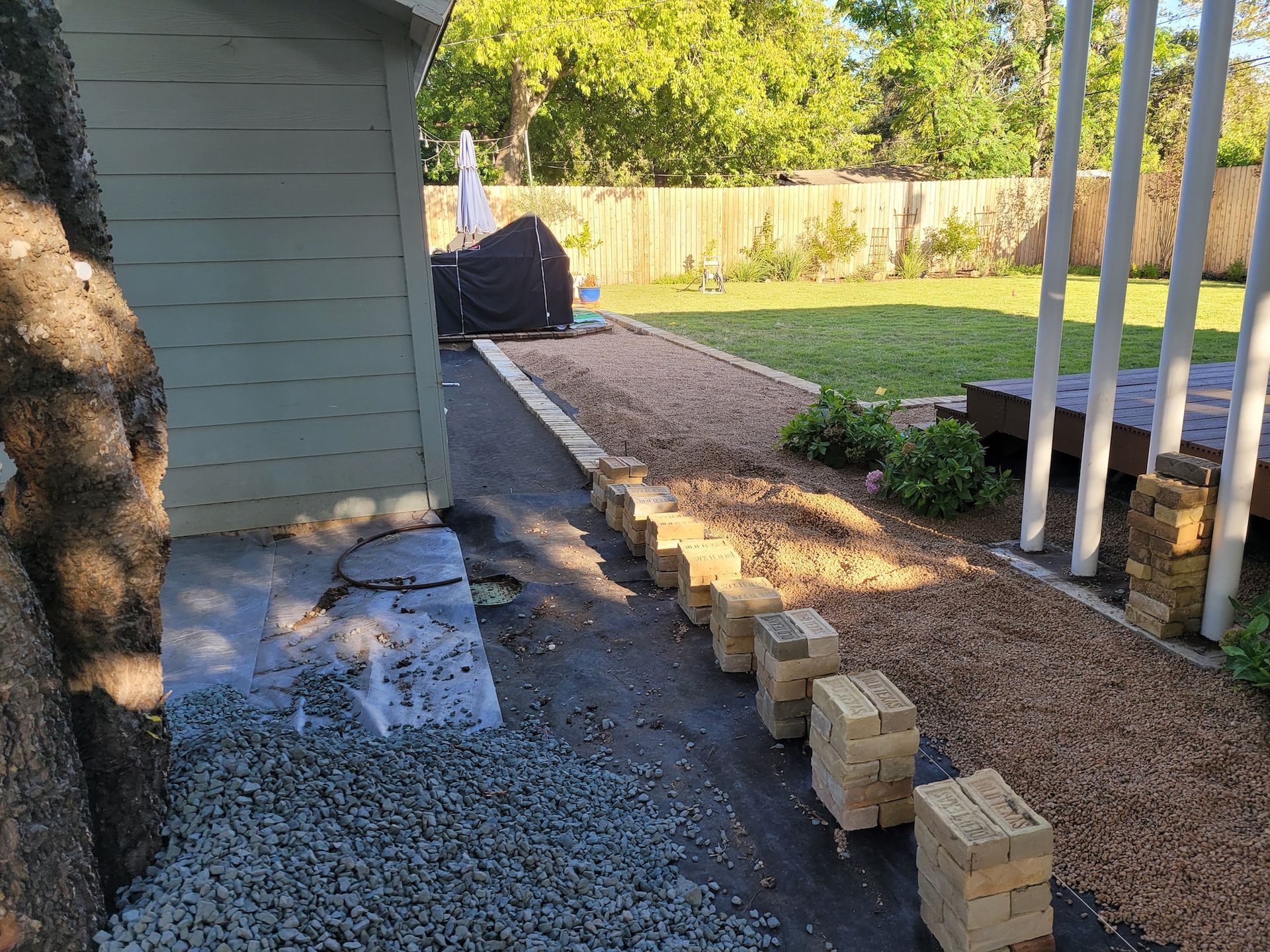 A row of bricks are sitting on the ground in a backyard next to a shed.
