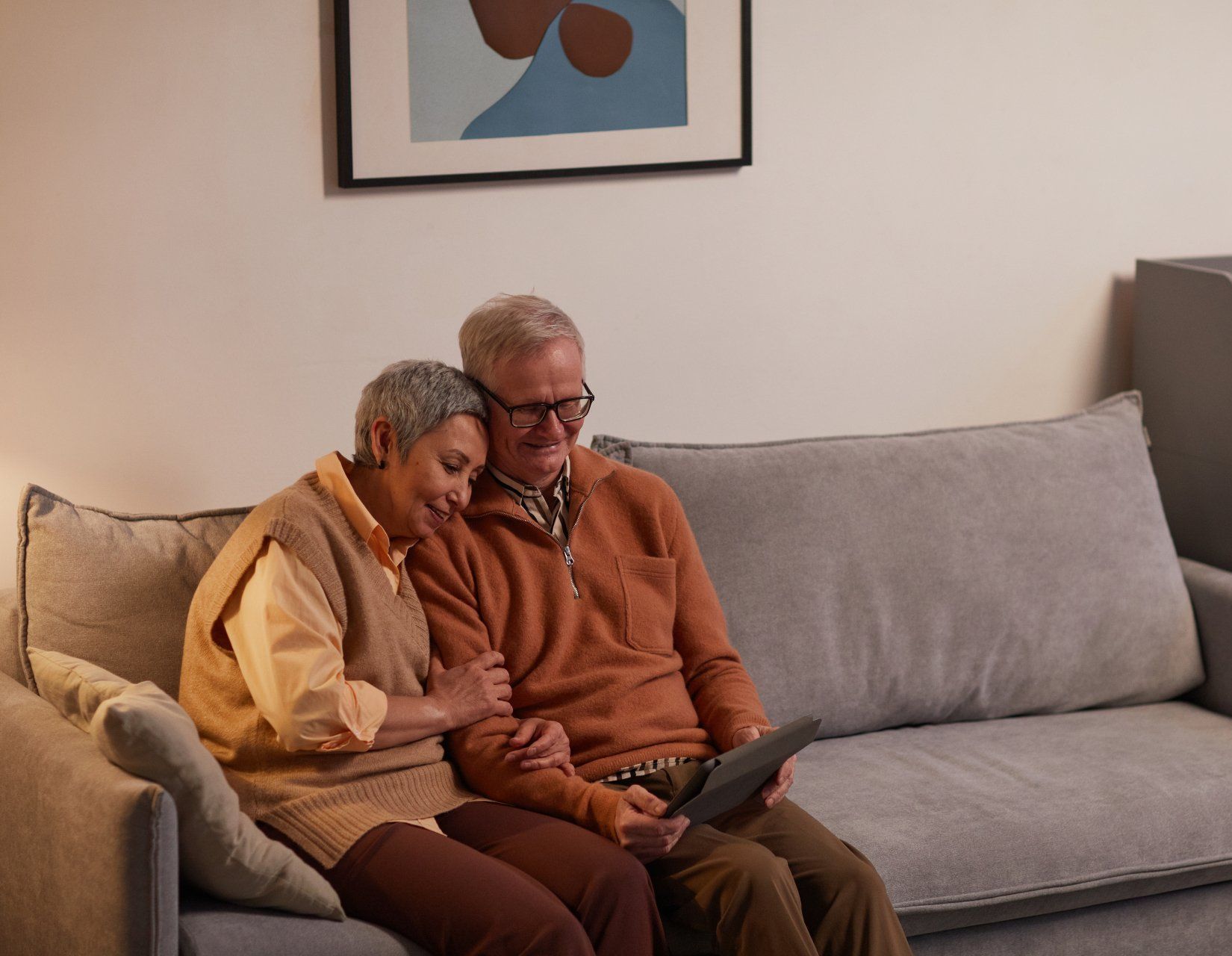 An elderly couple is sitting on a couch looking at a tablet.