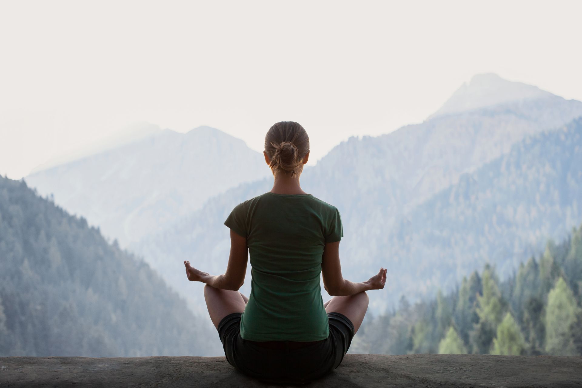 A person sits in a meditative pose facing a serene, misty mountain landscape.