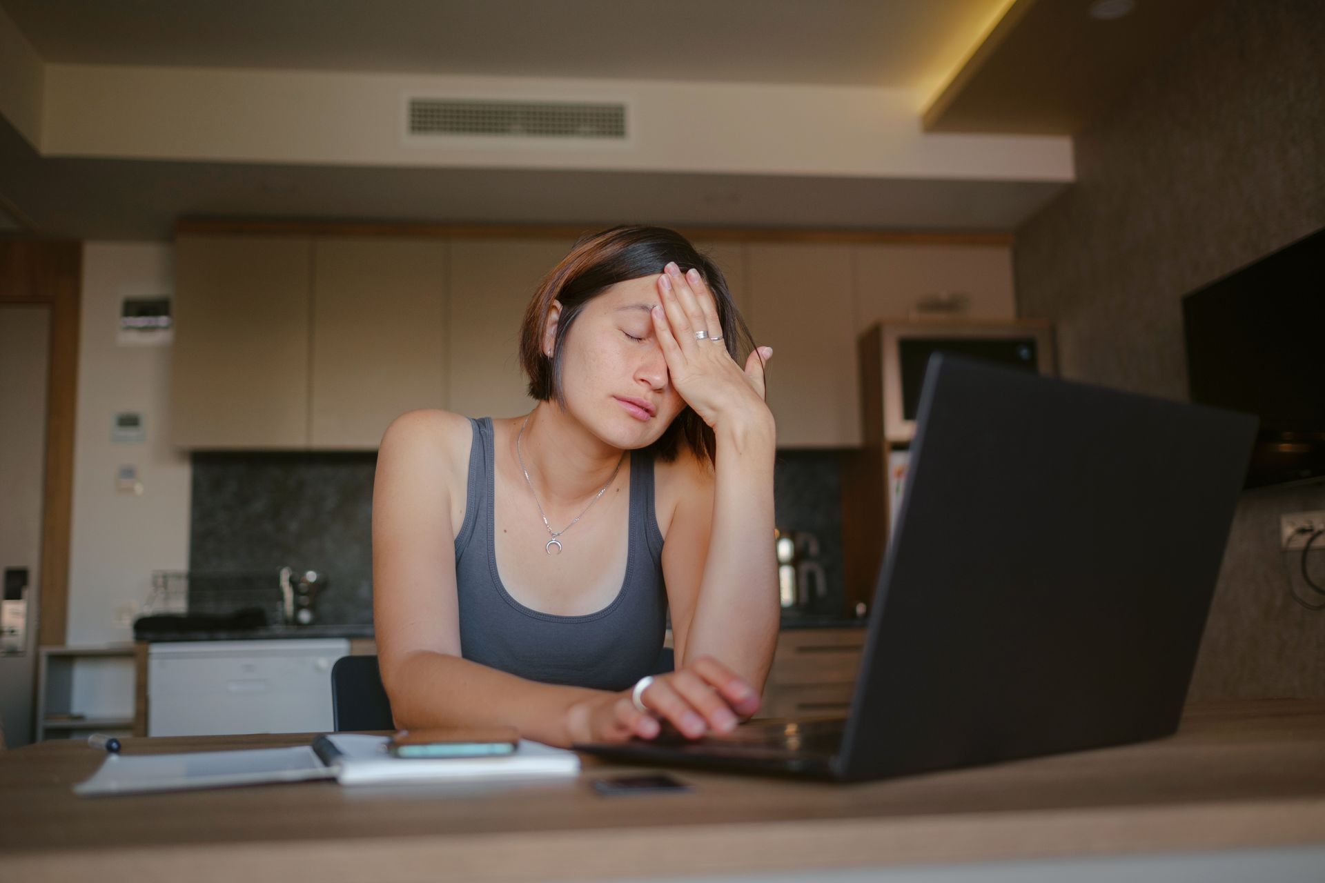 Person sitting at a table, face in hand, using a laptop in a kitchen