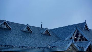 A sloping dark grey shingled roof with several triangular dormer windows under a pale, overcast sky.