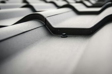 Close-up of a matte black metal roof with overlapping panels secured by a small screw.