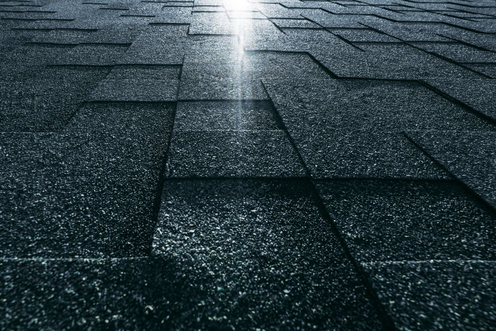 Wet dark rooftop shingles with a bright streak of light reflecting down the center