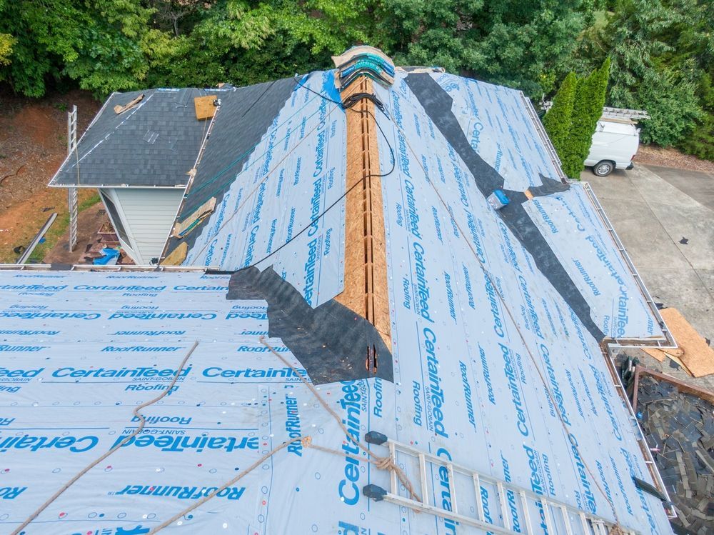 Roof under repair with blue underlayment, skylight, and visible chimney on a steep slope