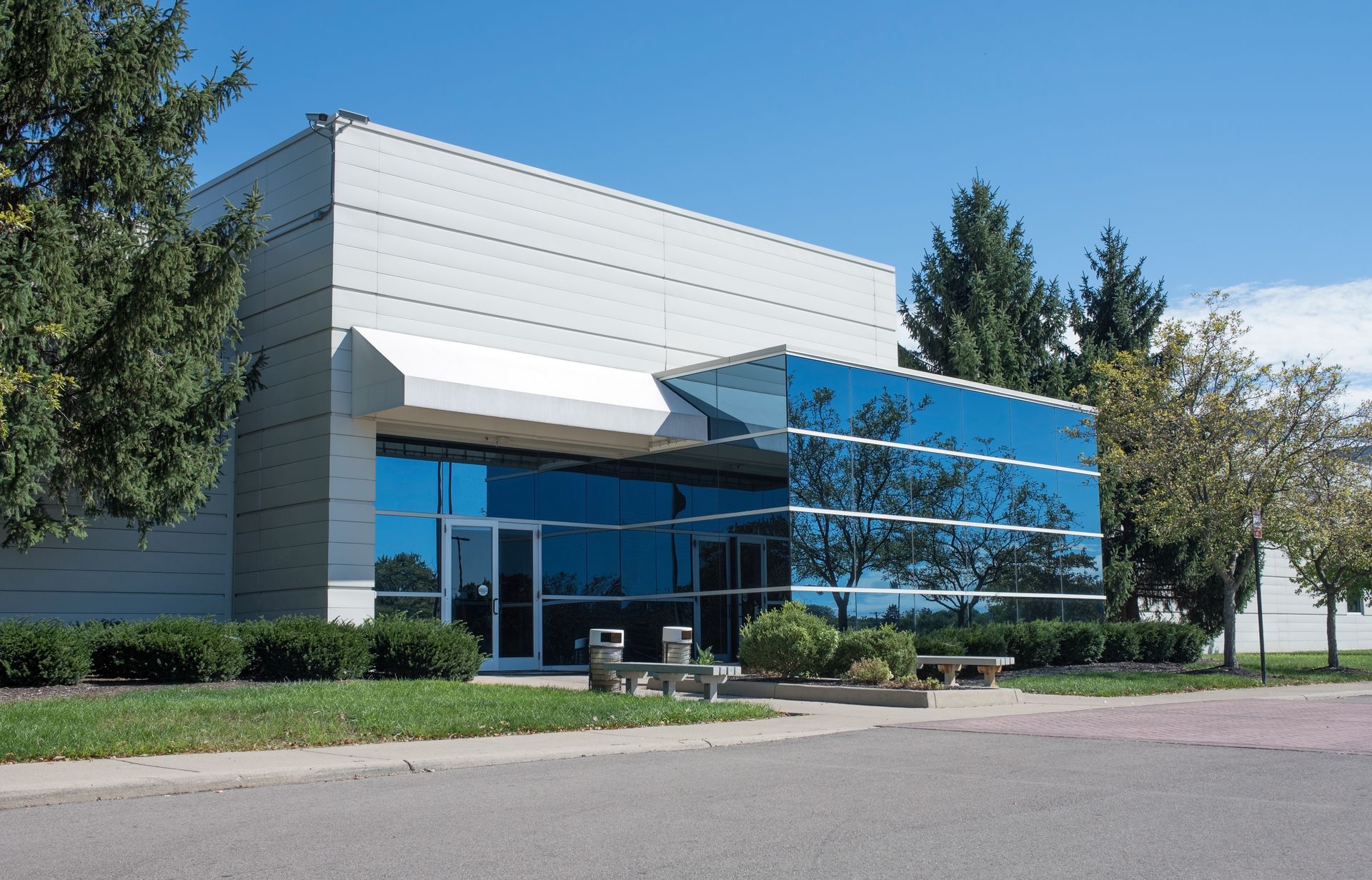 Modern commercial building with glass entrance, blue windows, gray walls, and landscaping.