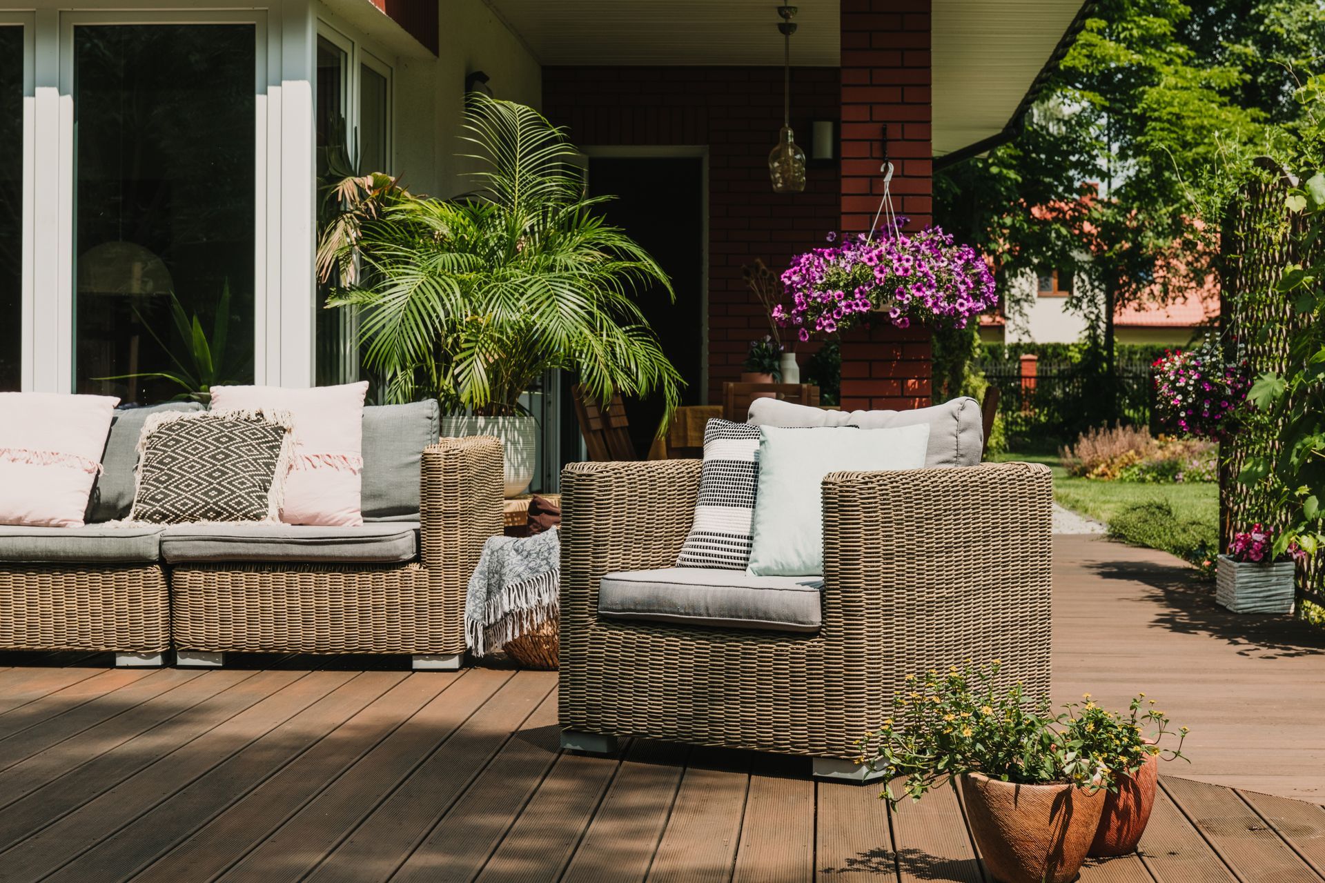 Wicker outdoor seating on a wooden deck with potted plants and colorful flowers.