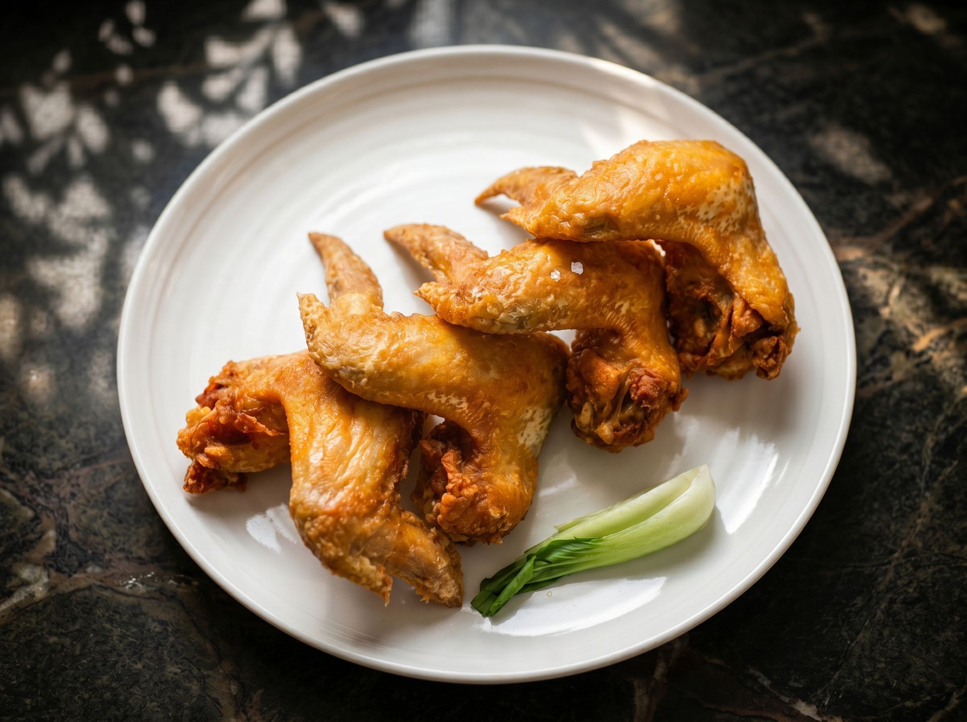 Plate of golden fried chicken wings with green garnish on a dark table