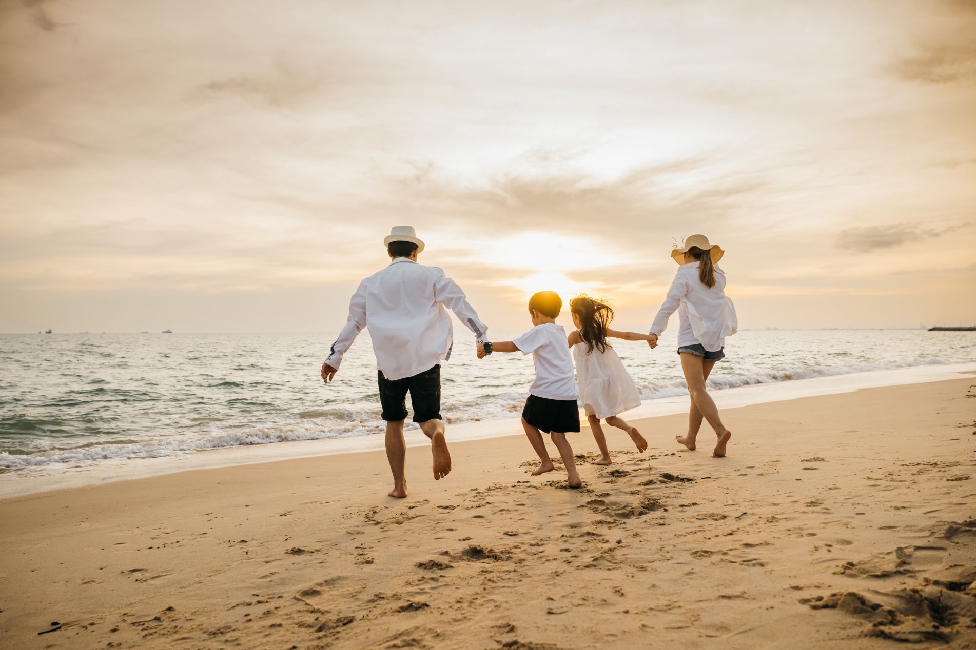Three people running hand in hand on a sandy beach at sunset, with waves in the background