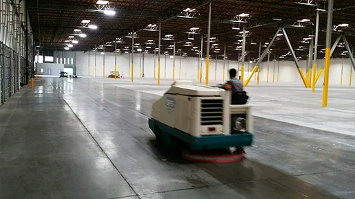 Industrial warehouse aisle with a person driving a small floor-cleaning machine