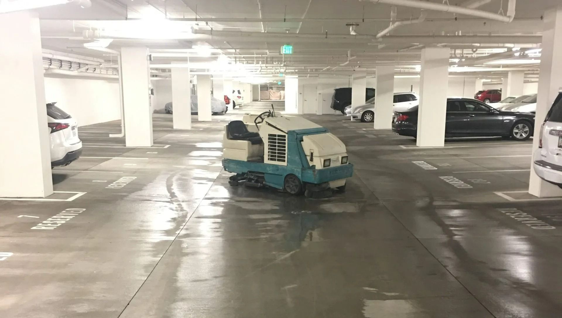 Small teal utility vehicle driving through a wet underground parking garage.