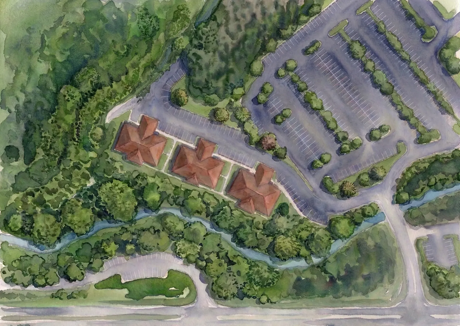 Aerial view of a building complex with red roofs beside a parking lot and tree-lined roads.