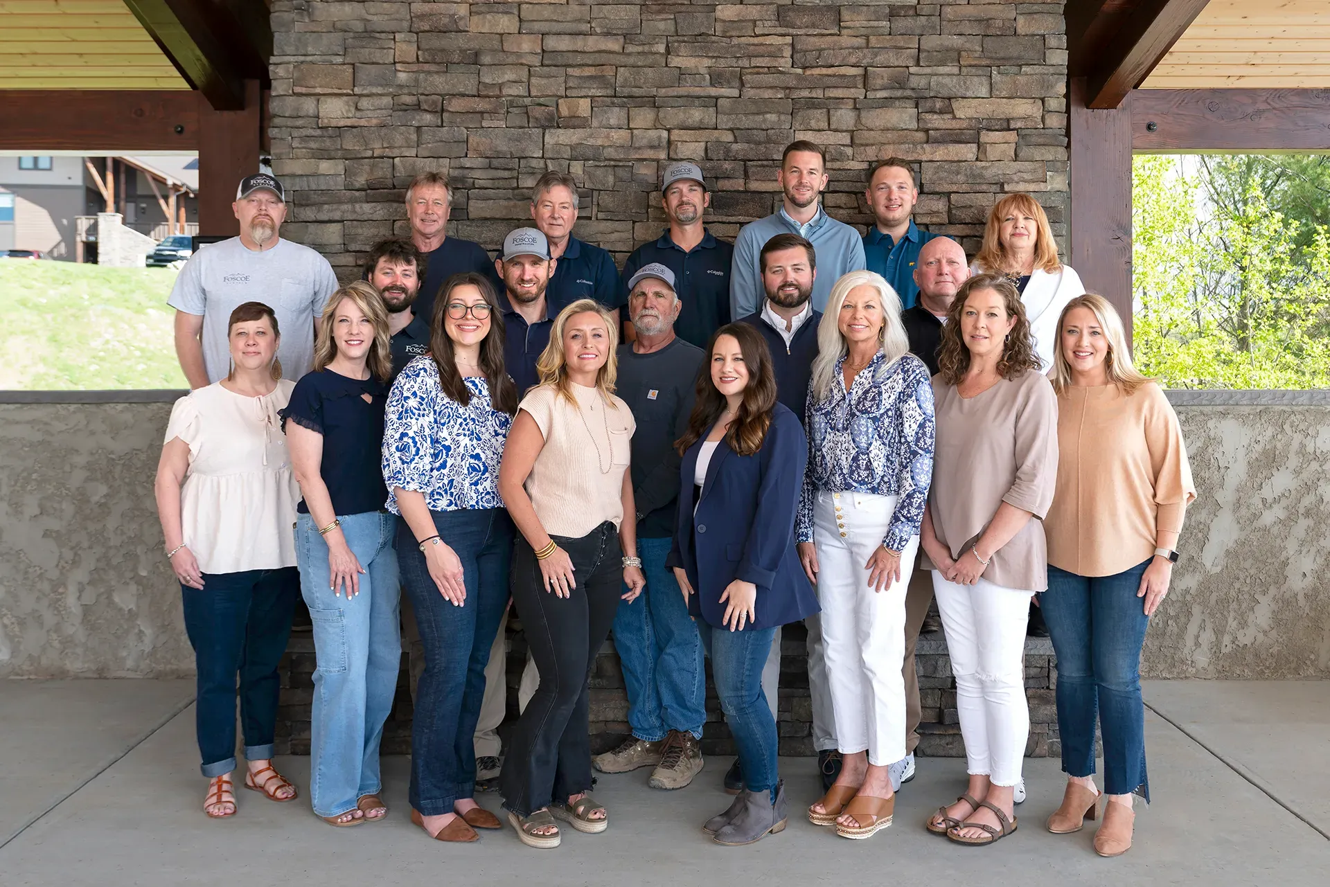 Group of 15 adults posing together outdoors under a covered stone structure.