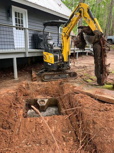 A yellow excavator is digging a hole in the ground in front of a house.
