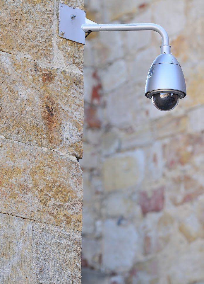 A security camera is mounted on the side of a stone wall.