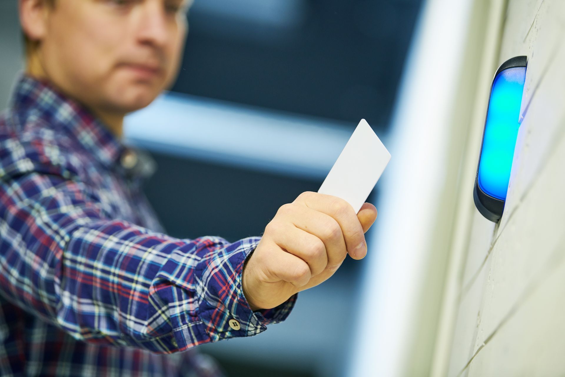Man in plaid shirt using a card to access a blue-lit security reader.