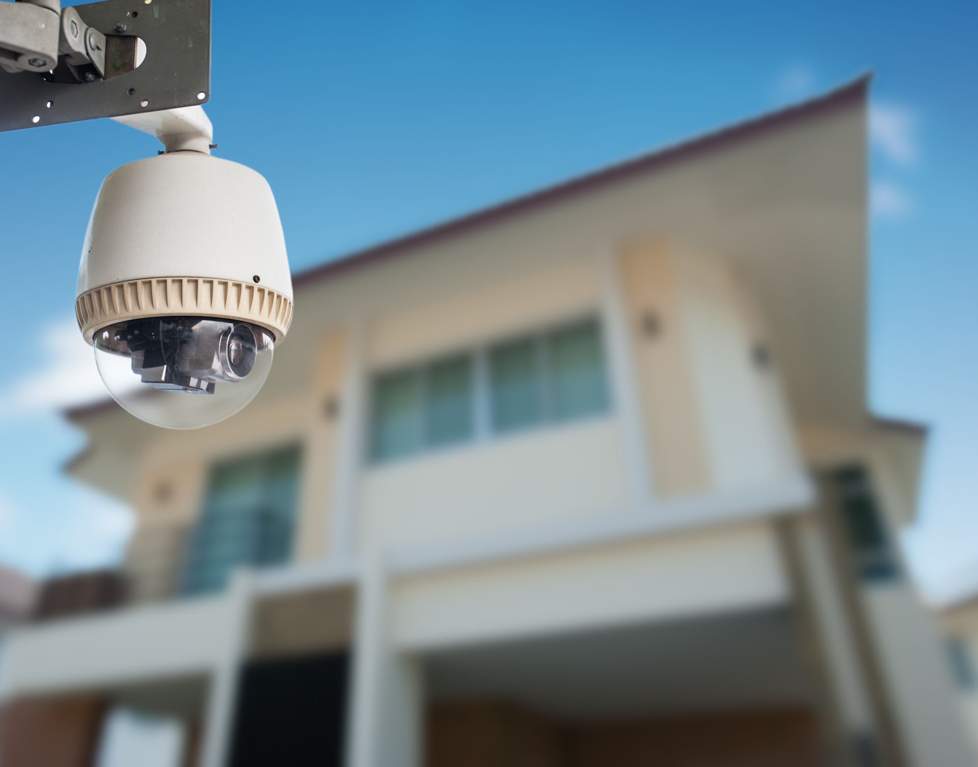 A security camera is hanging from a pole in front of a house.