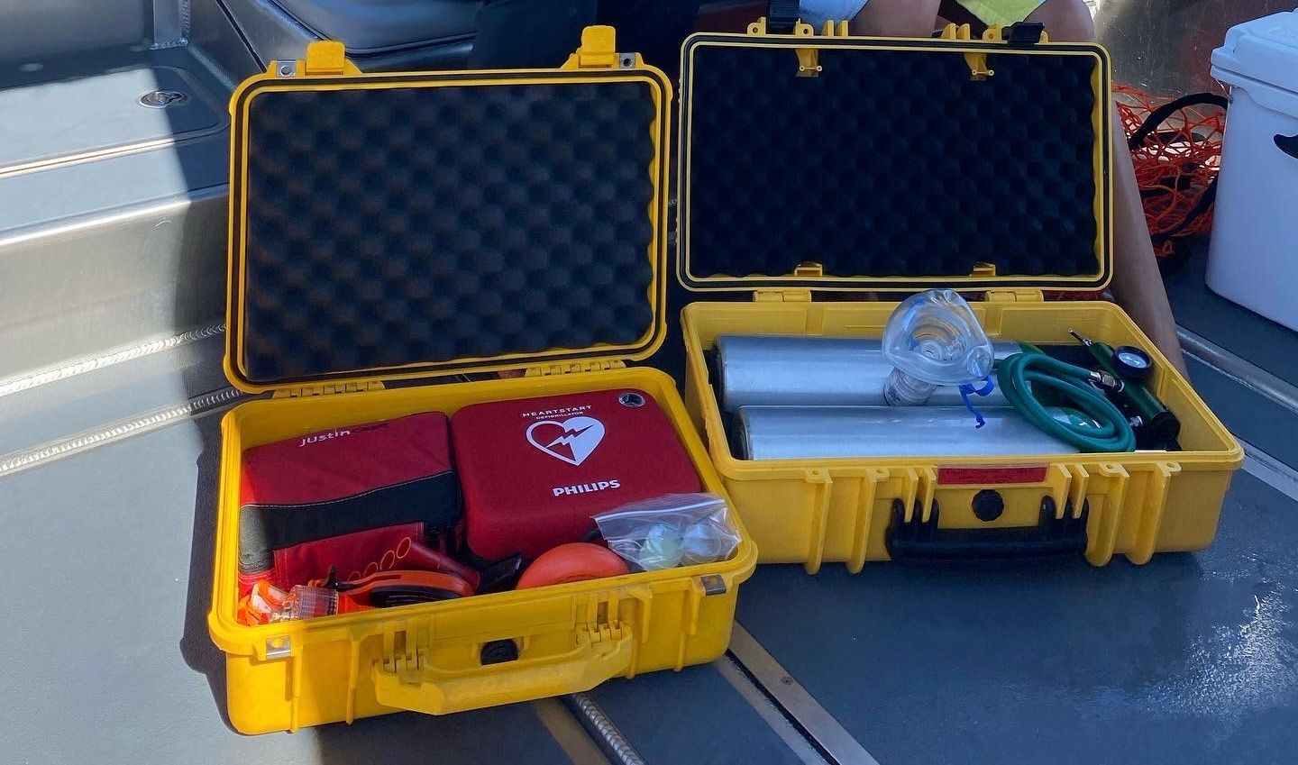 Two open yellow cases on a dock, one with red gear and one with a metal tube and green hose.
