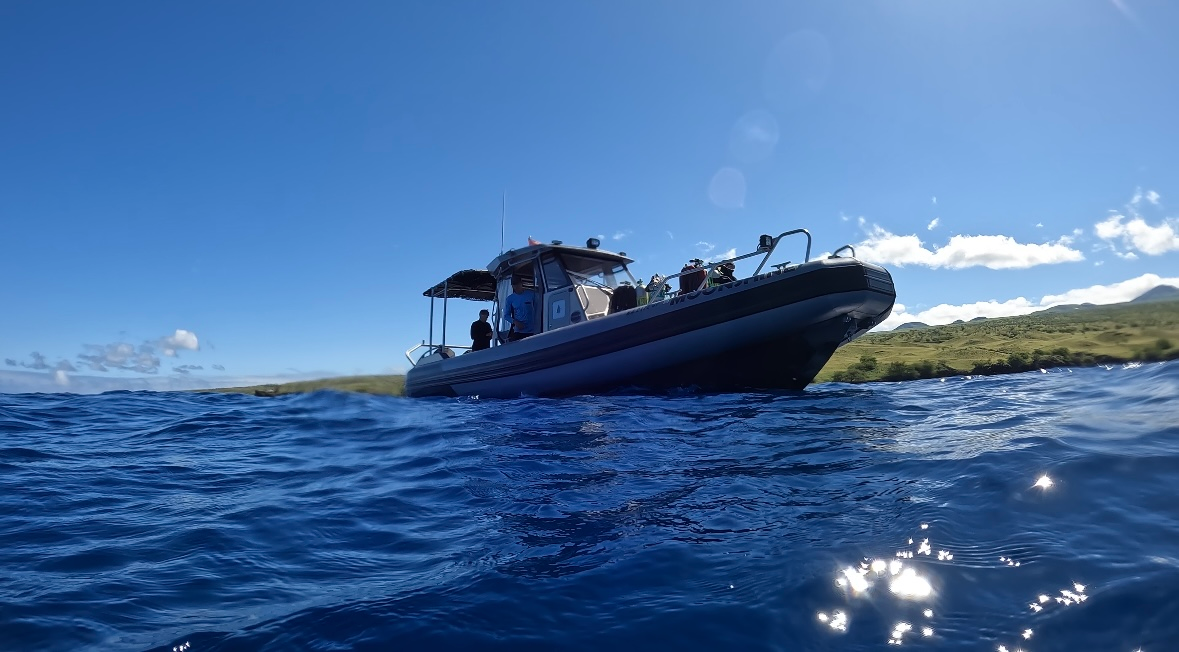 Large dark boat on rough blue ocean under a bright sky, shot from the waterline