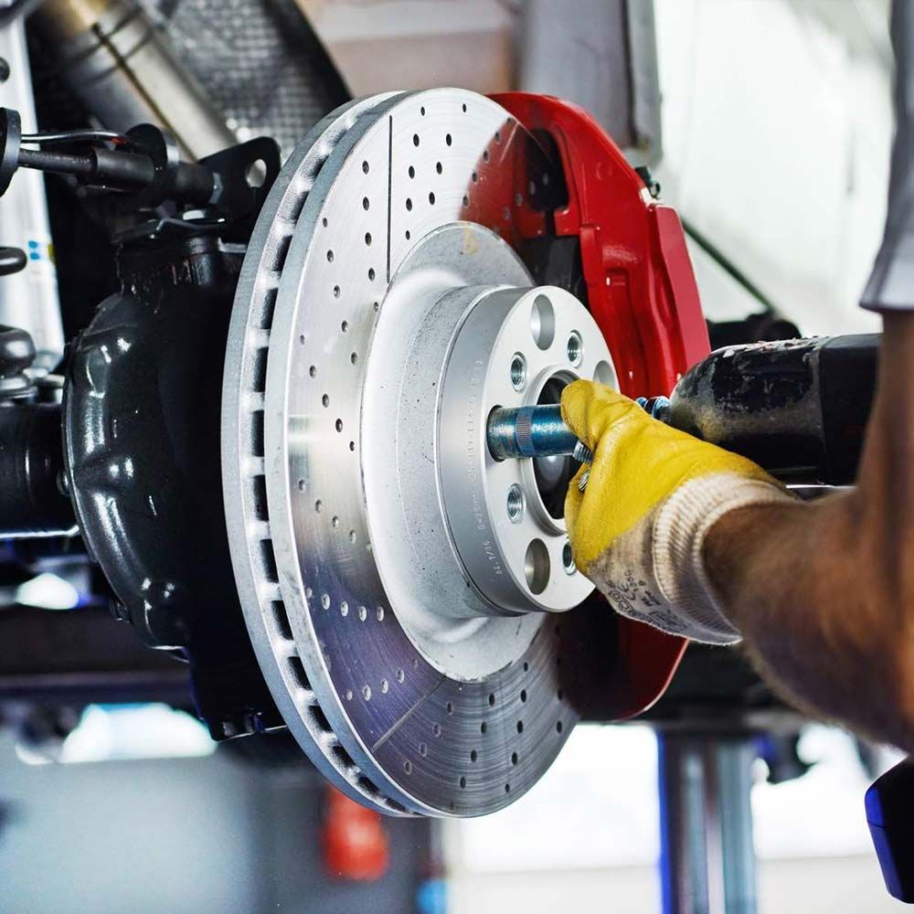 Mechanic in yellow gloves installing a silver brake rotor on a red car hub