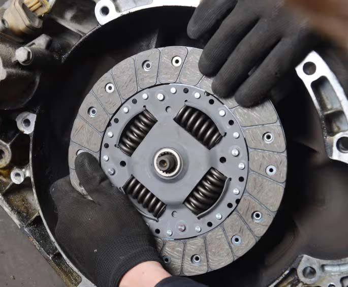 Gloved hands holding a car clutch disc inside a vehicle transmission assembly