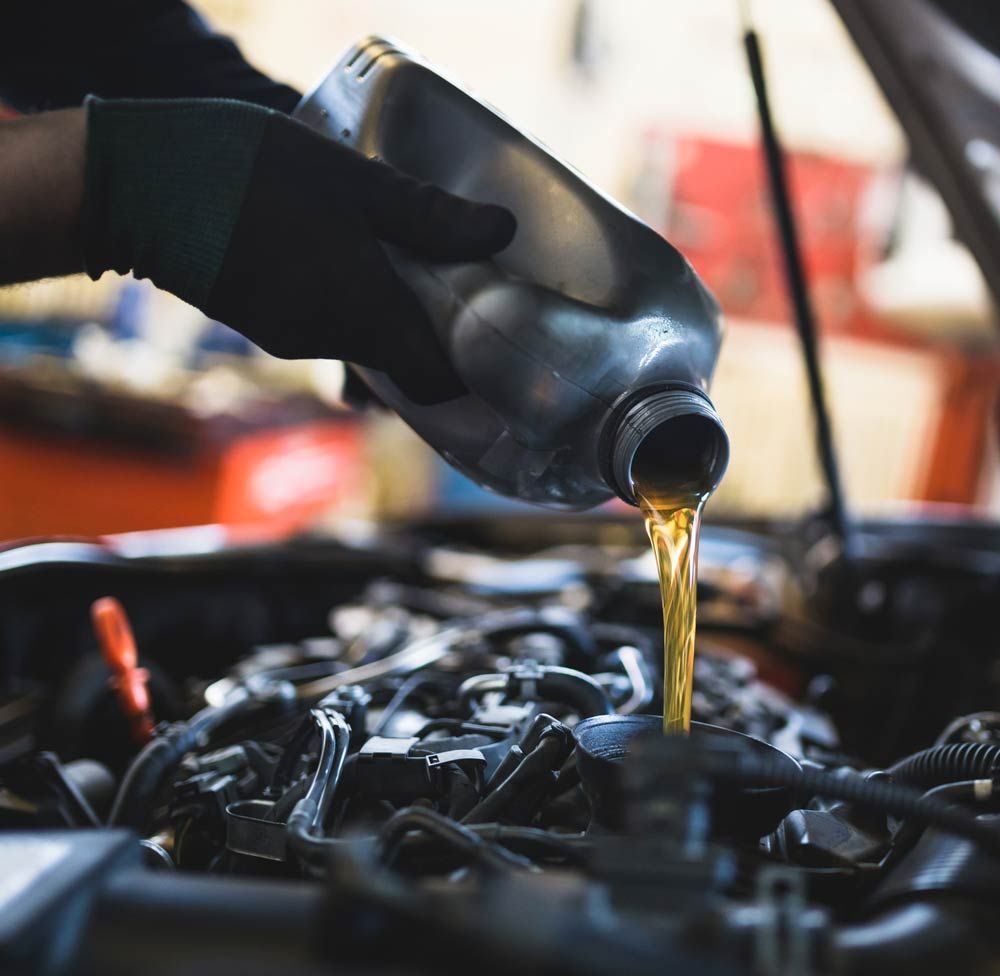 Motor oil being poured from a bottle into a car engine in a garage