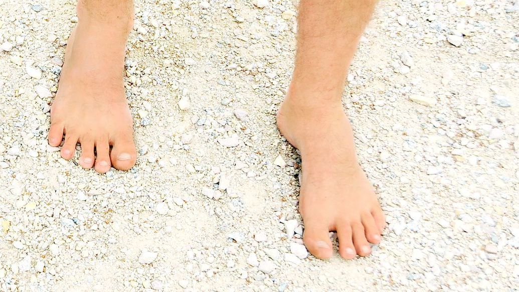 A person's bare feet are standing on a white sandy surface.