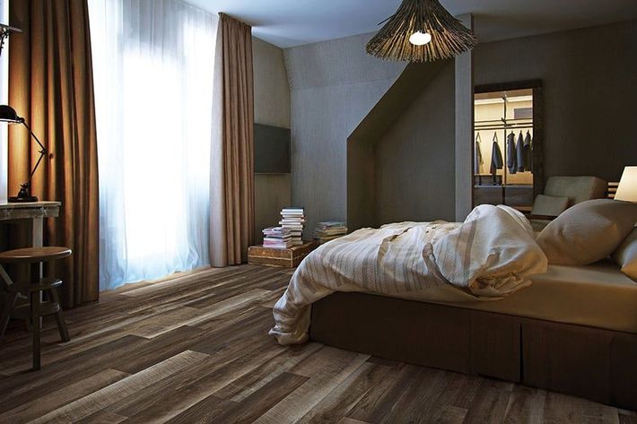 Modern bedroom with a made bed, sheer curtains, wooden floor, and warm hanging lamp