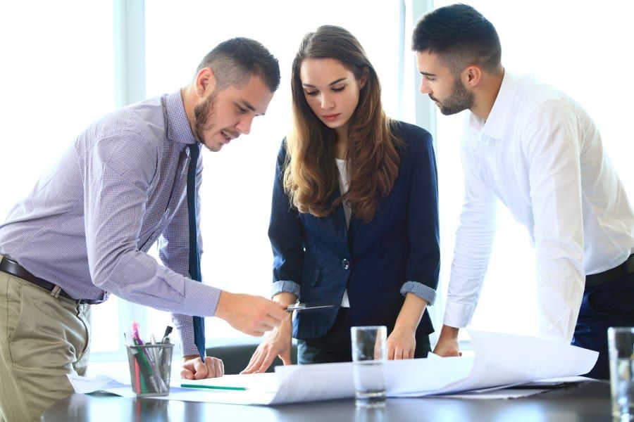 Three coworkers reviewing documents together at a desk in a bright office