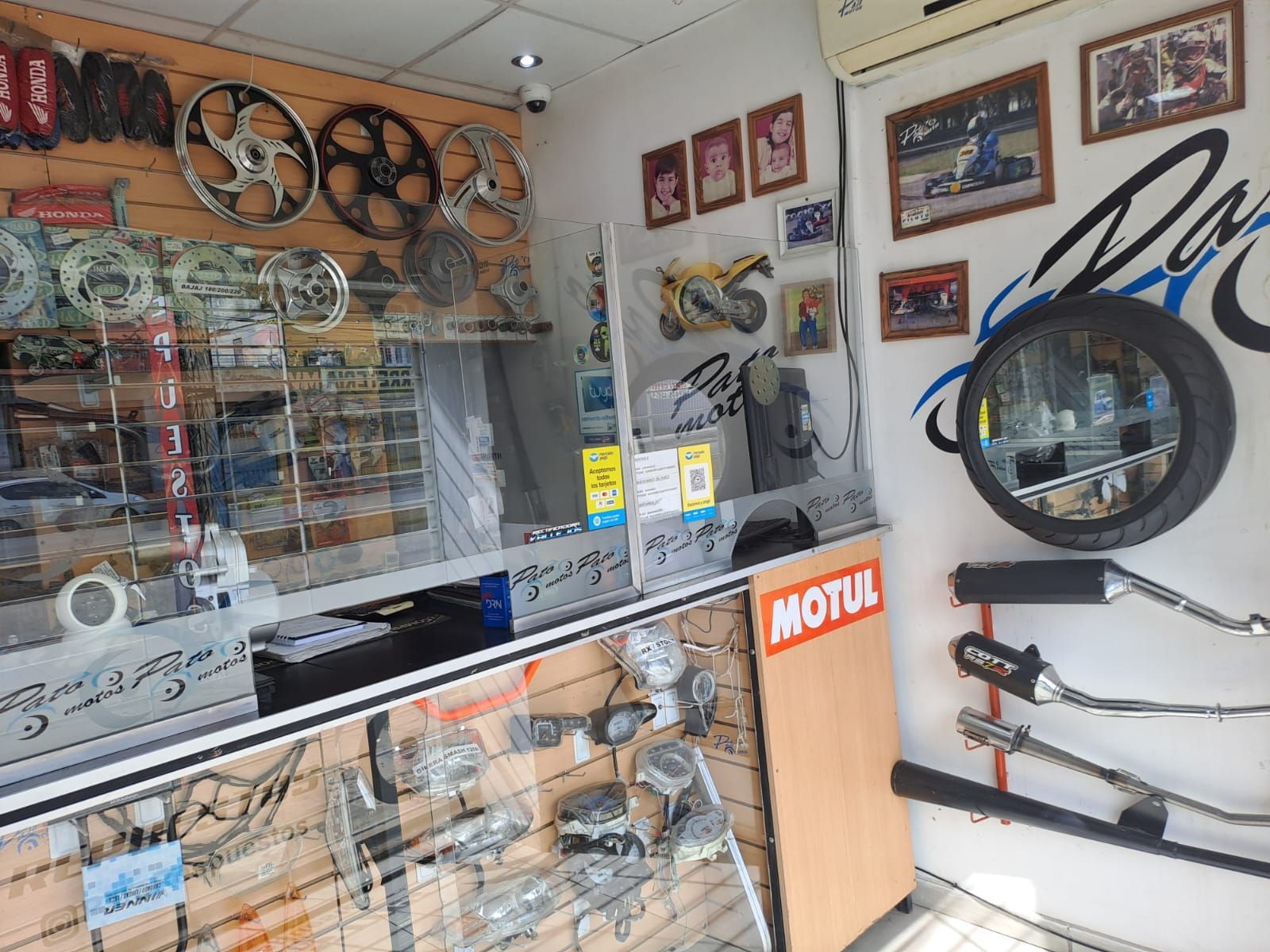 Mostrador de una tienda de motos con cascos, repuestos, ruedas y fotos enmarcadas en las paredes