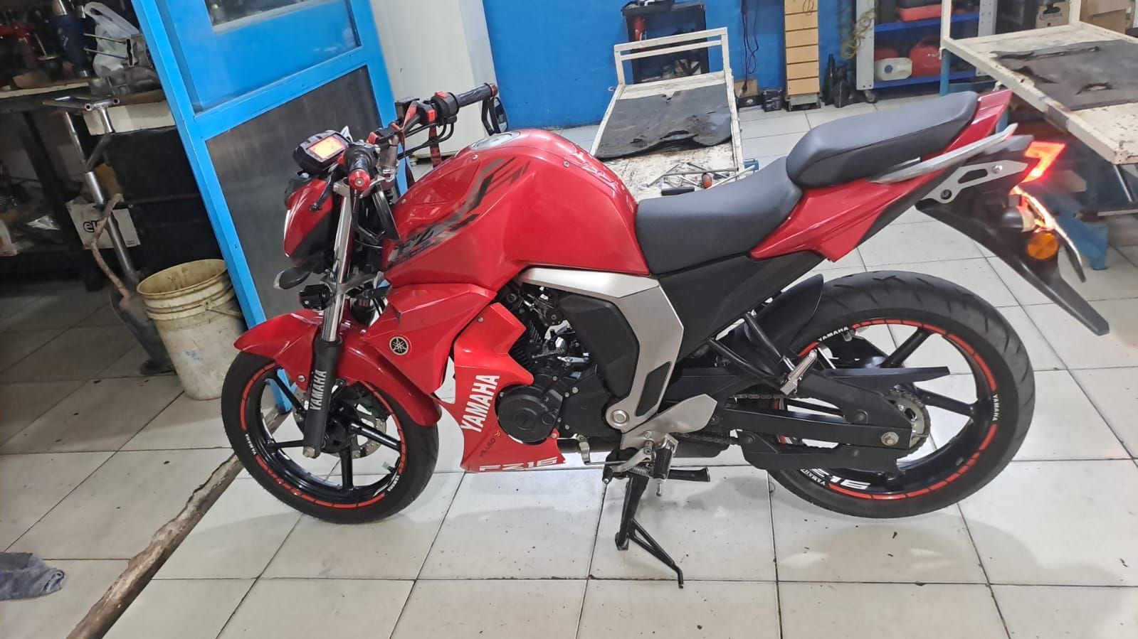 Motocicleta deportiva roja aparcada en el interior, sobre un suelo de baldosas, vista de lado.