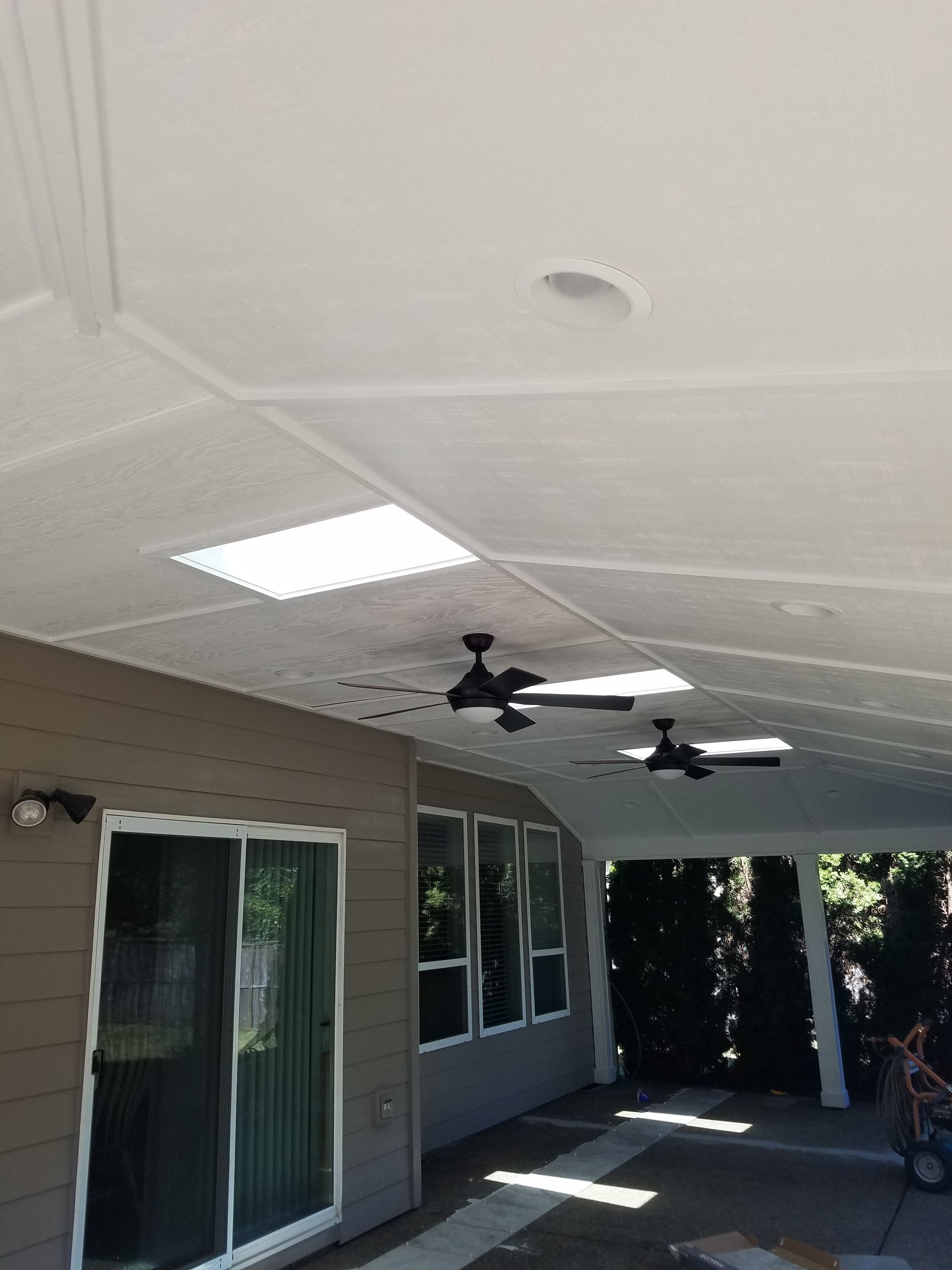 Covered patio with a white ceiling, skylight, and ceiling fans. A sliding glass door and windows are visible.