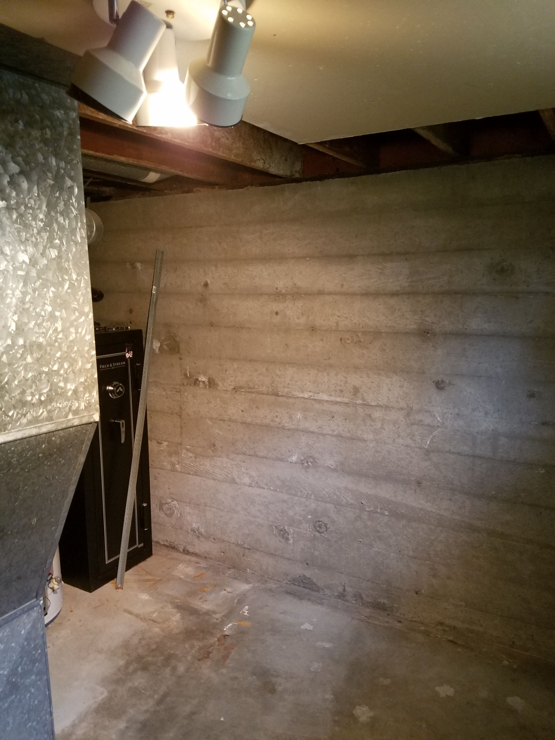 Basement with concrete wall, exposed beams, and a black metal door. The floor is concrete.
