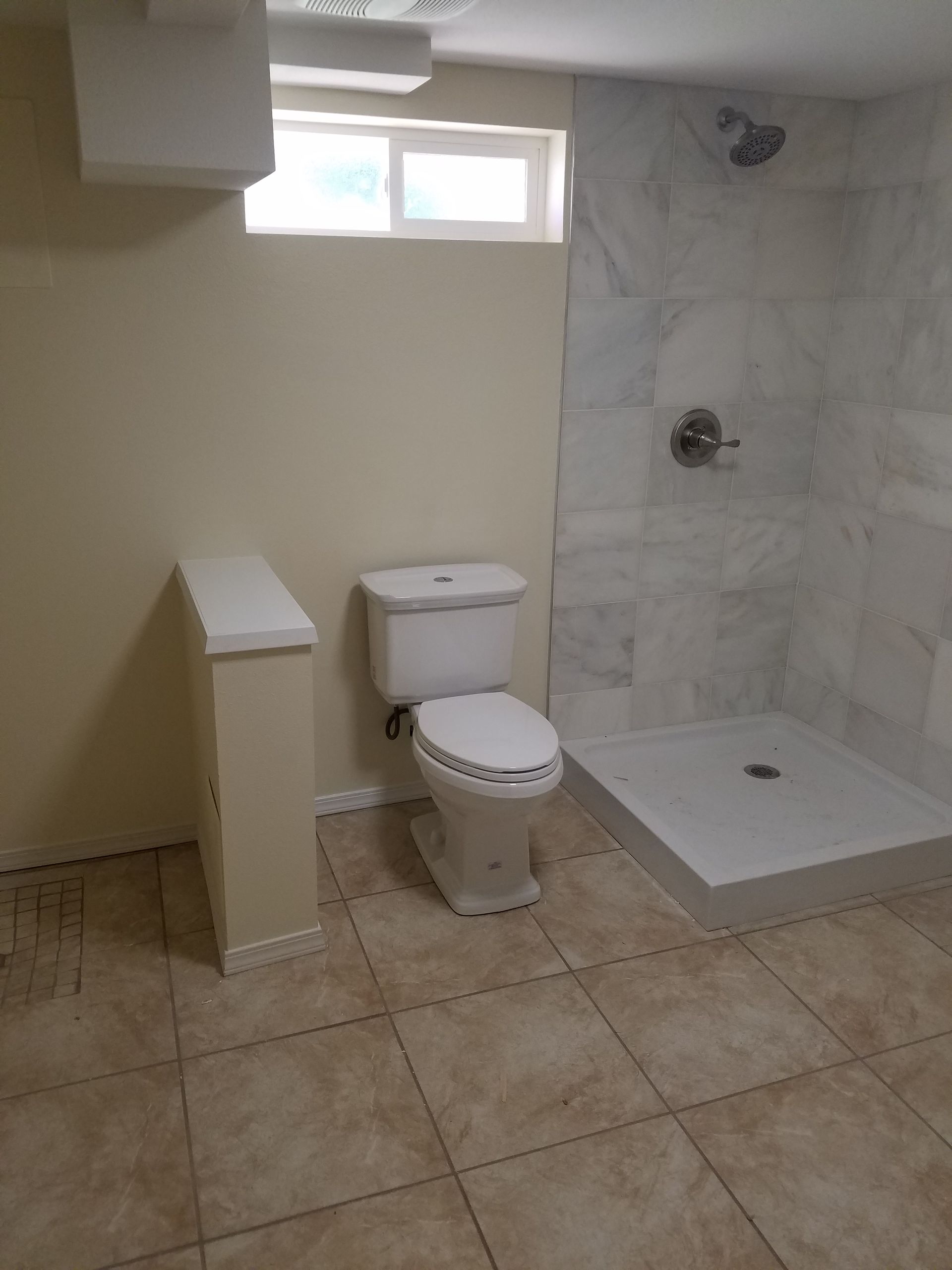 Bathroom with toilet and shower, beige walls and tile floor.