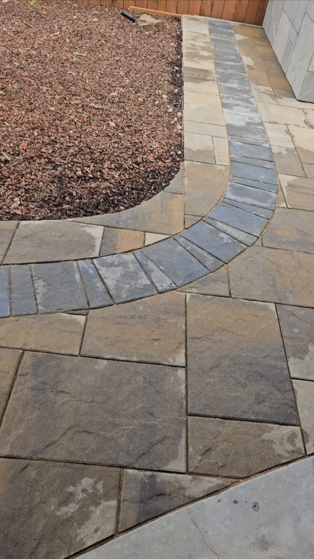 Curved stone walkway beside a gravel garden bed and wooden fence