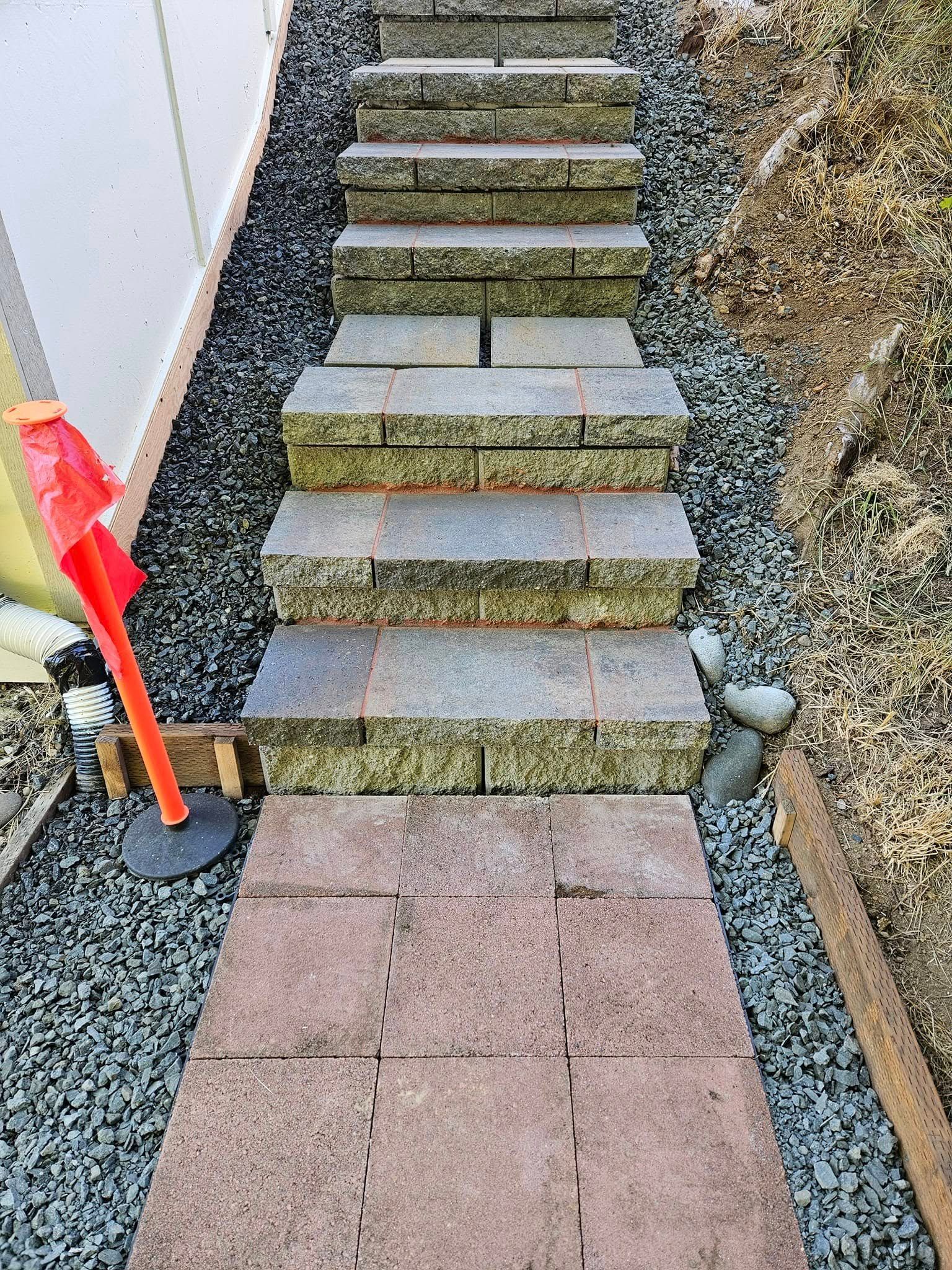Steep outdoor stone steps between gravel walls, with a red marker post at the bottom.