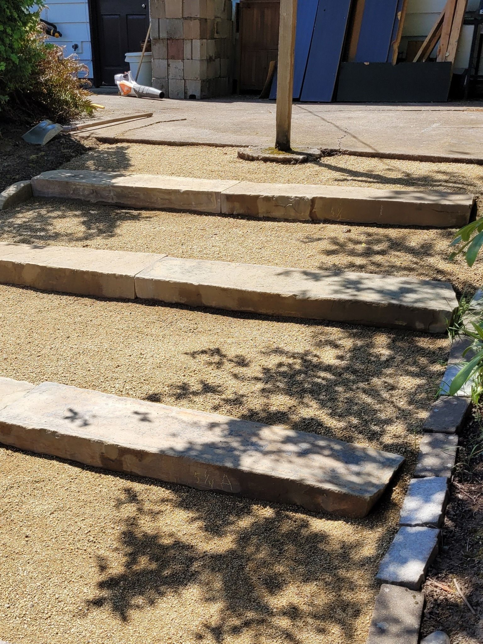 Outdoor stone steps leading to a building entrance, with gravel paths and sunlight casting shadows
