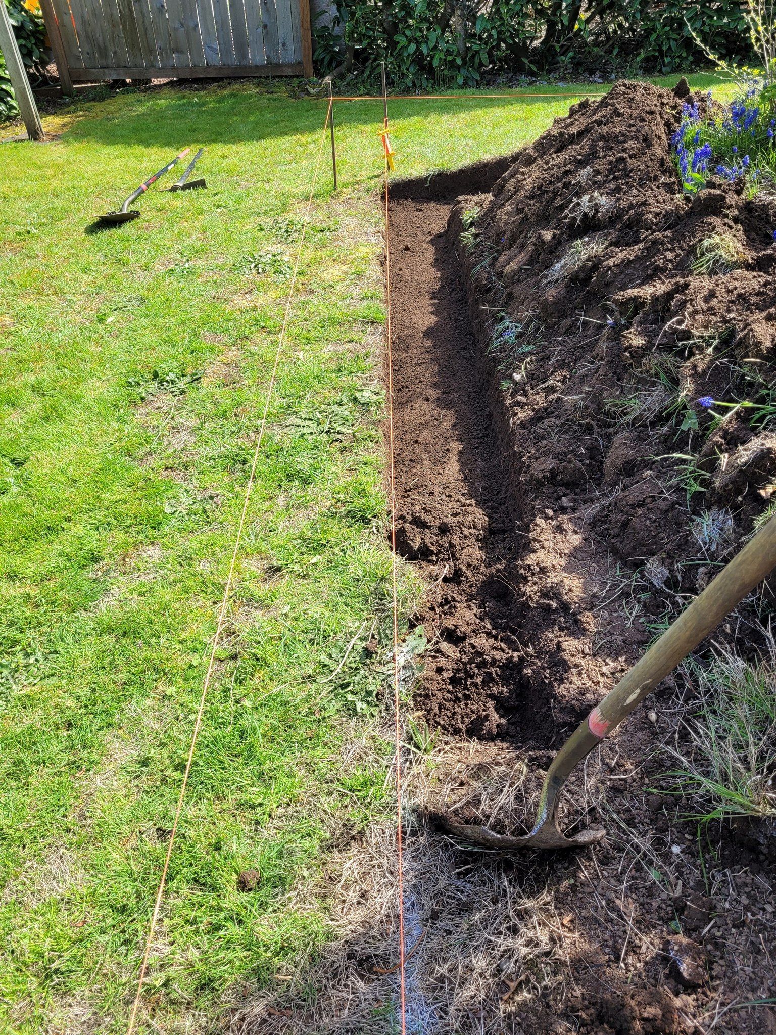 Garden bed being dug beside a grassy lawn, with a shovel and a mound of soil along the edge