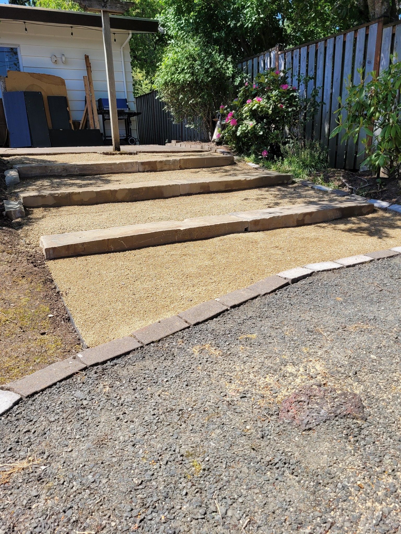 Gravel path with three concrete steps leading to a porch beside a fence and trees