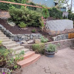 Narrow stone walkway beside a curved brick retaining wall in bright sunlight, with a handrail shadow across it