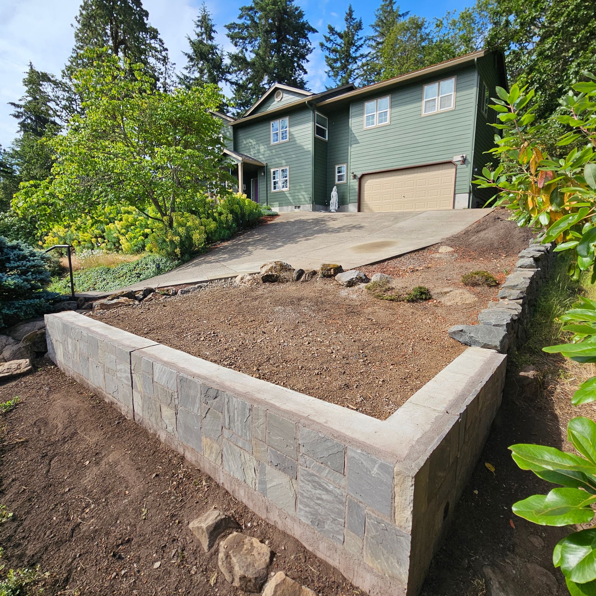 House with sloped driveway and stone retaining wall in a landscaped yard.