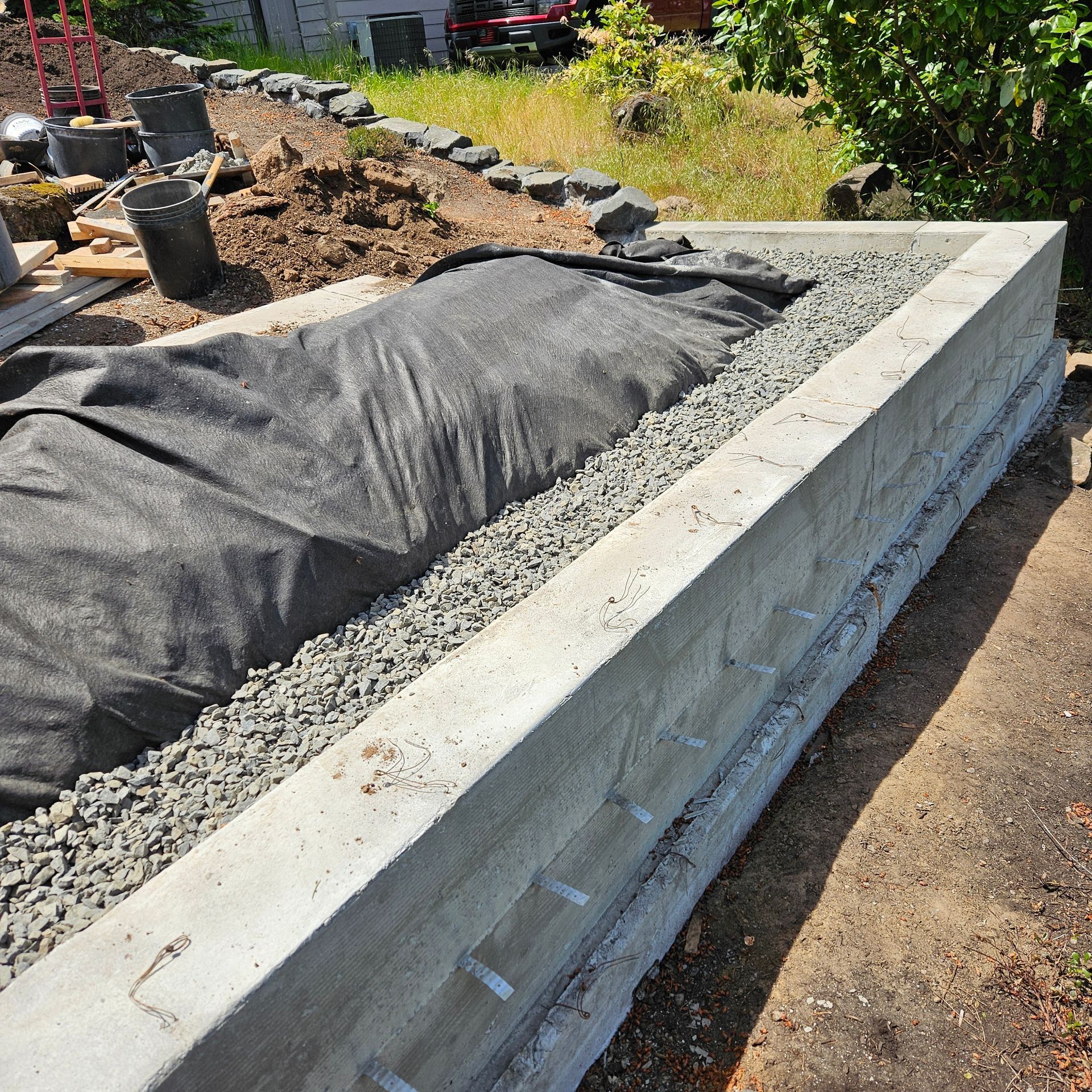 Long concrete retaining wall under construction beside a dirt garden bed