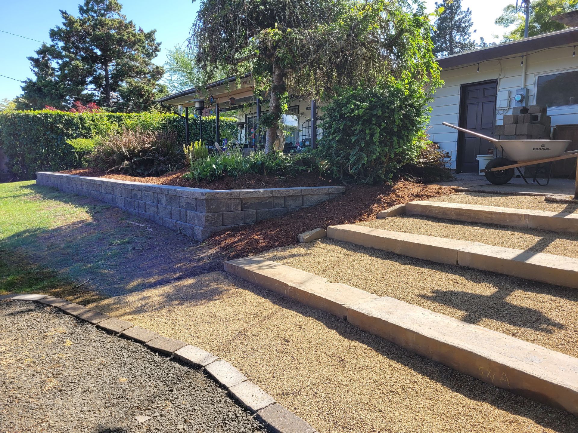 Concrete steps leading to a house entrance with a landscaped retaining wall and garden bed.
