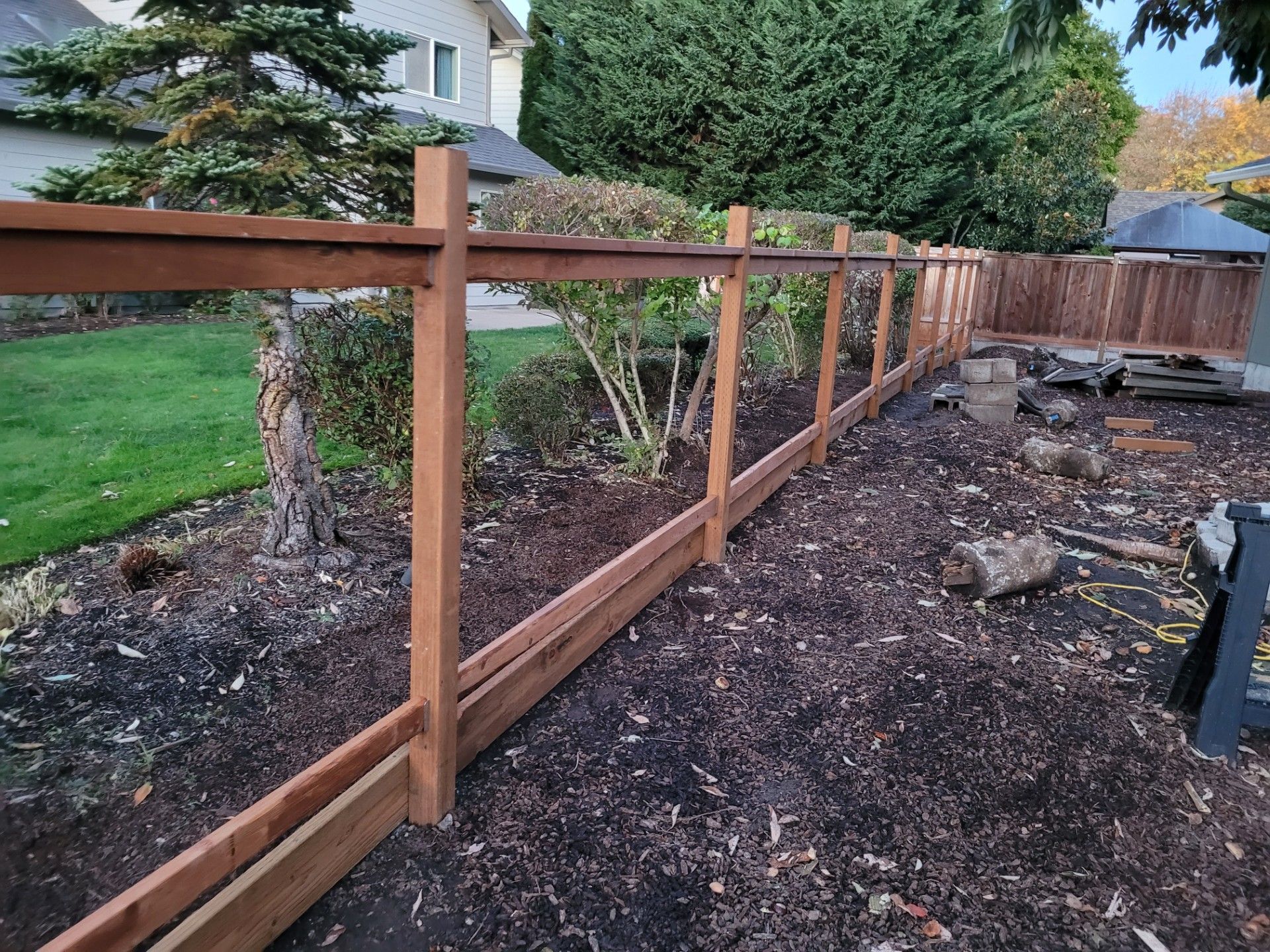 Wooden backyard fence under construction beside a lawn and garden beds