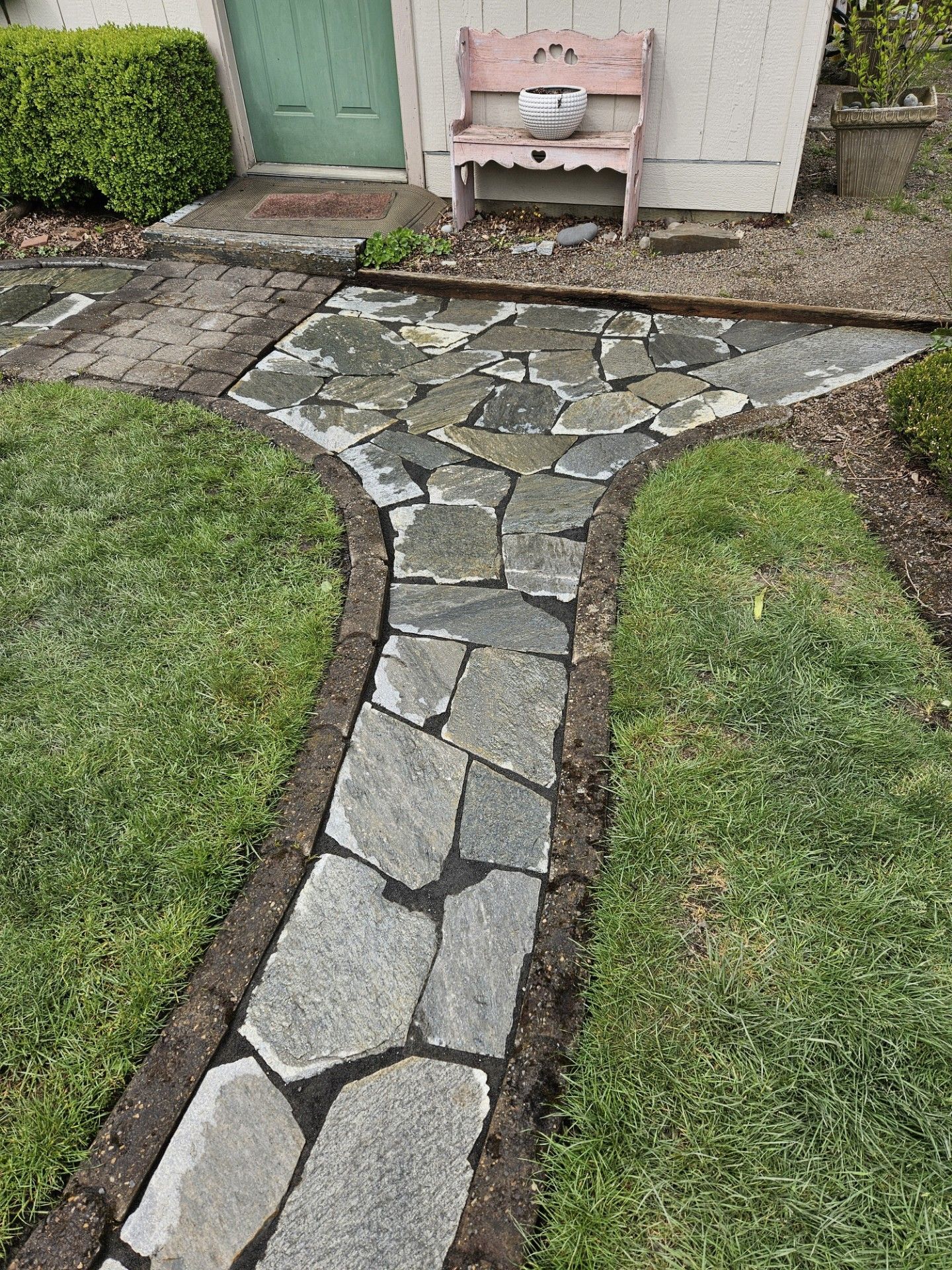 Stone walkway leading to a house door, bordered by grass with a small outdoor sink ahead