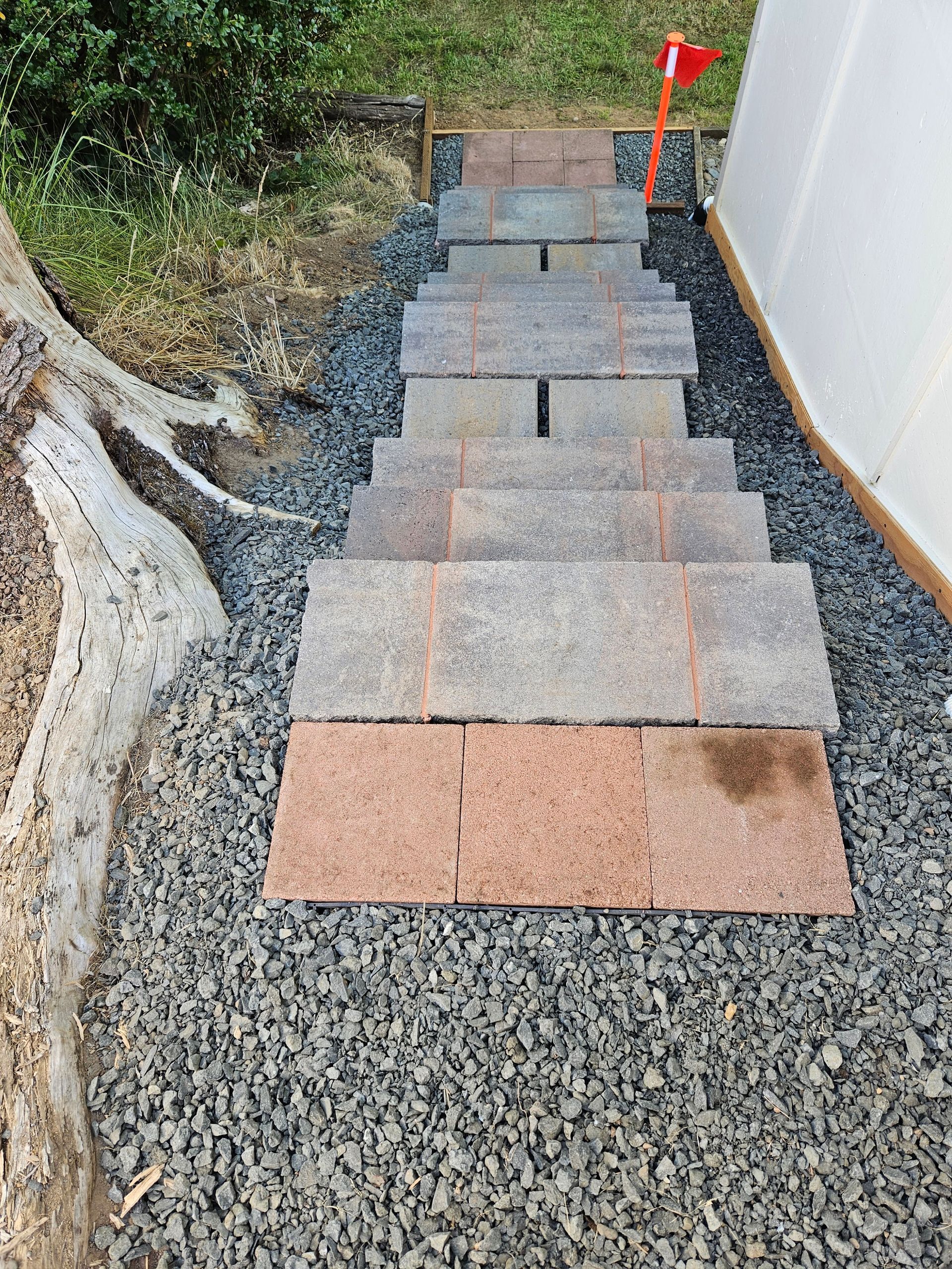 Stepped gravel path with stone pavers beside a white wall, bordered by exposed soil and red flags at the top.