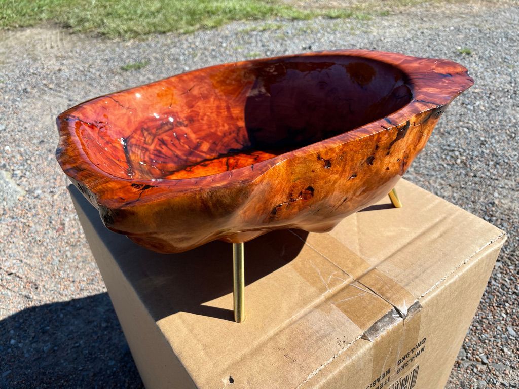 Wooden bowl with gold legs, atop a cardboard box, outdoors.